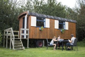 Een houten pipowagen en mensen aan tafel op een boerencamping drenthe